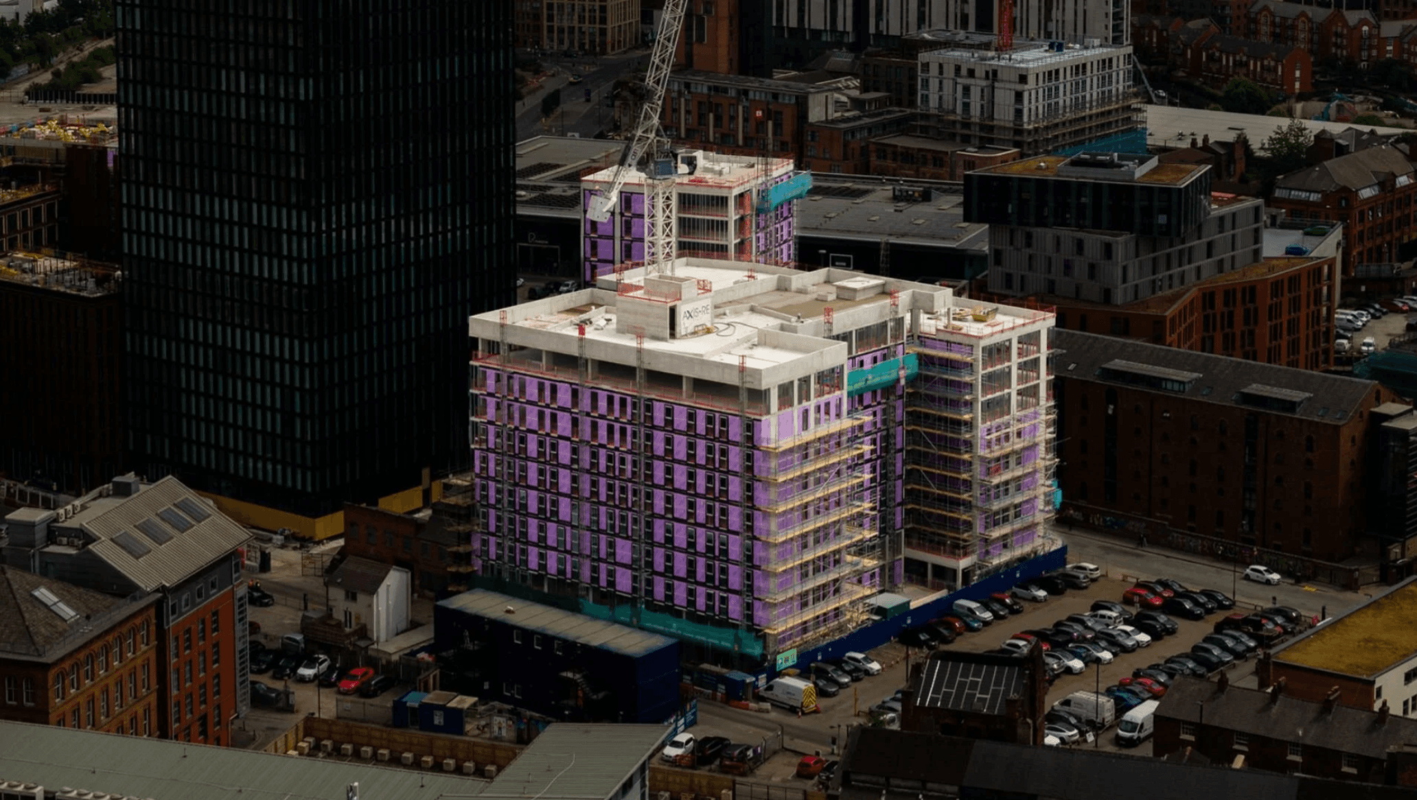 1NQ, Tariff Street, Manchester: aerial photo of the scheme under construction with purple Tyvek-membrane wrap, completed roof level and tower crane, surrounded by Manchester rooftops