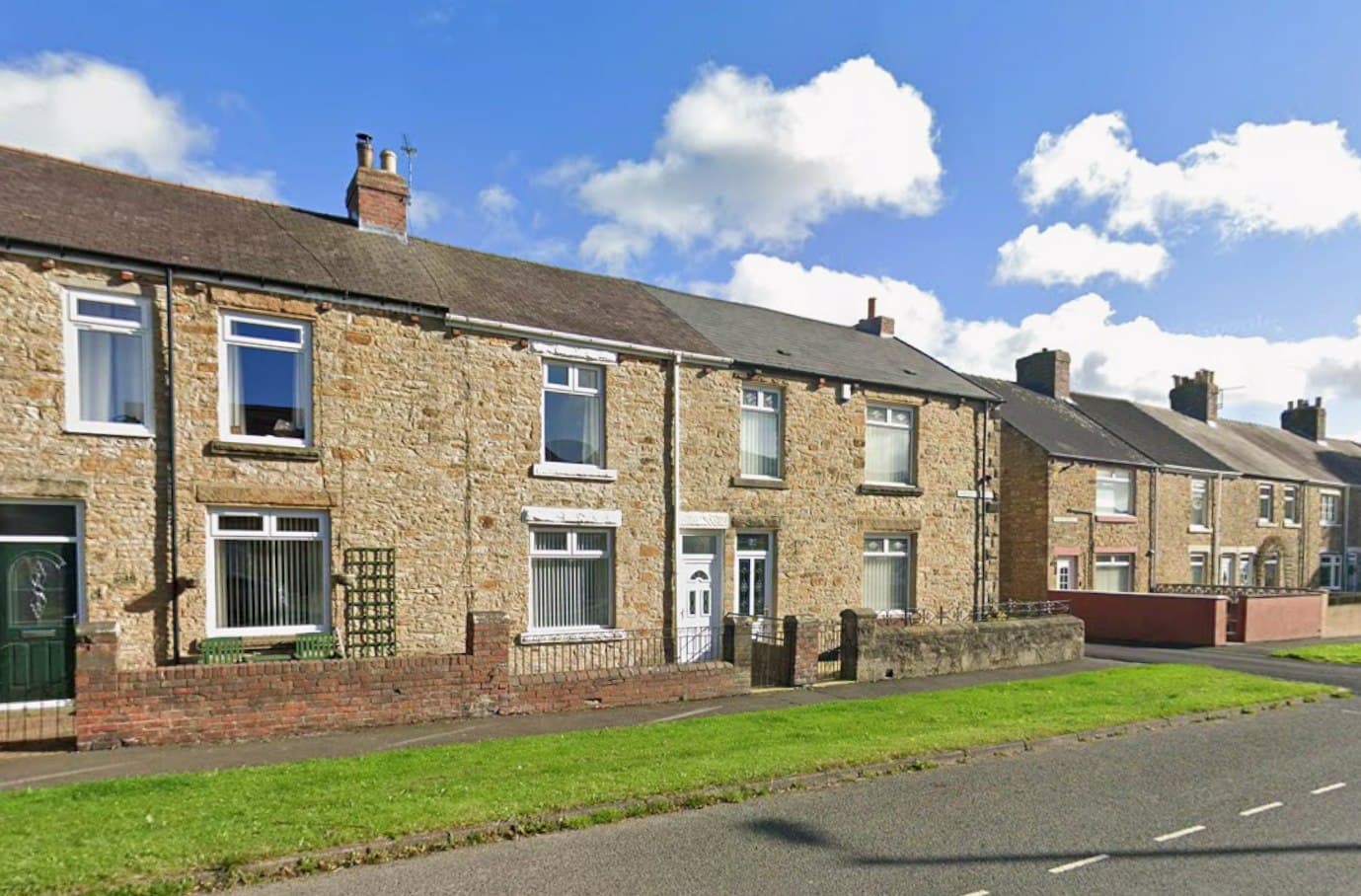 Annfield Plain, County Durham: traditional stone-built two-storey terraced homes running along the street under a bright sky, with neighbouring brick terraces beyond, Karbon Homes affordable scheme