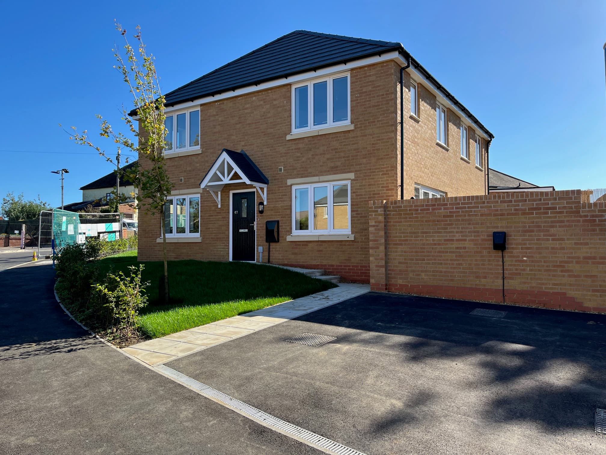 Central Avenue, Northampton: completed three-bedroom yellow-brick detached house with grey-slate gabled roof and timber porch canopy, paved driveway and walled boundary, slim young tree on the front garden in clear morning sun