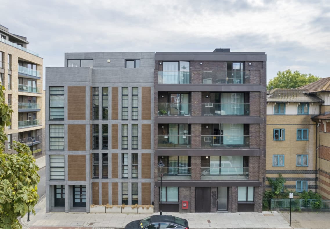 Grange Walk Cladding Remediation, Bermondsey: completed five-storey infill block in grey-brick frame with timber-clad bays and dark-anthracite balconies, sandwiched between a cream-rendered neighbour and a yellow-brick mansion block