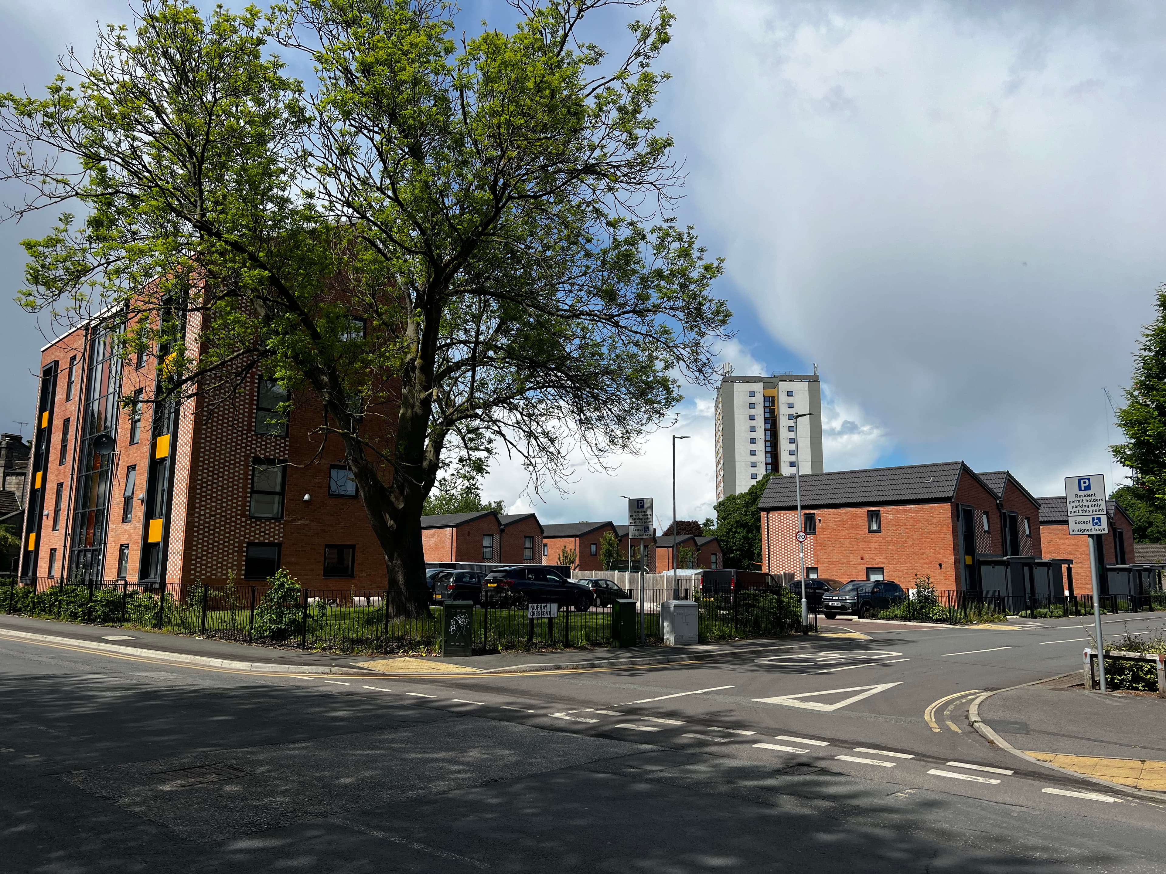 Leeds Meynell, Holbeck: wide street view from the junction approaching the scheme, apartment block on the left, the new houses ranged along the road, mature tree in the foreground and a Holbeck residential tower visible in the distance.