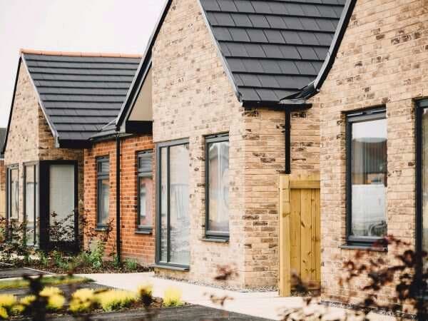 Newbridge Village, Hull: completed yellow-brick single-storey bungalows with anthracite-slate gable roofs, large picture windows and timber gate detail
