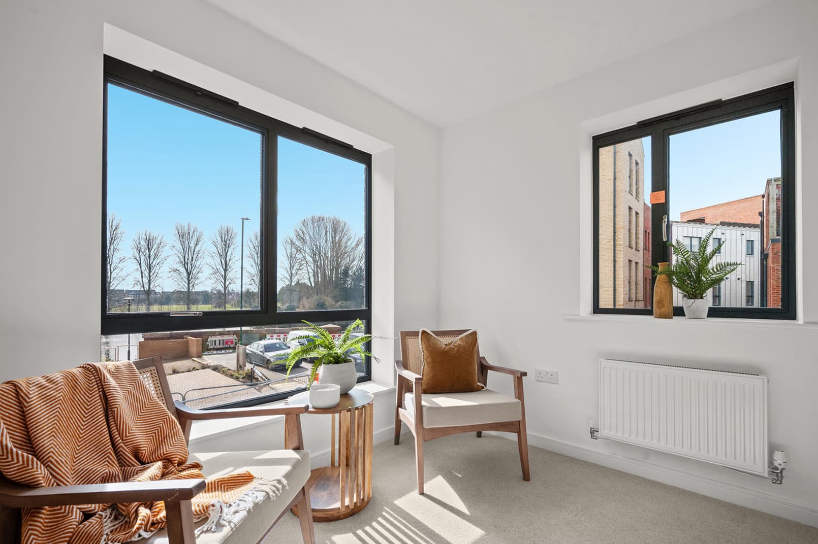 Pelham Waterside, Nottingham: completed interior, bright living corner with armchair, throw and side table, large picture window framing tree-lined waterside view