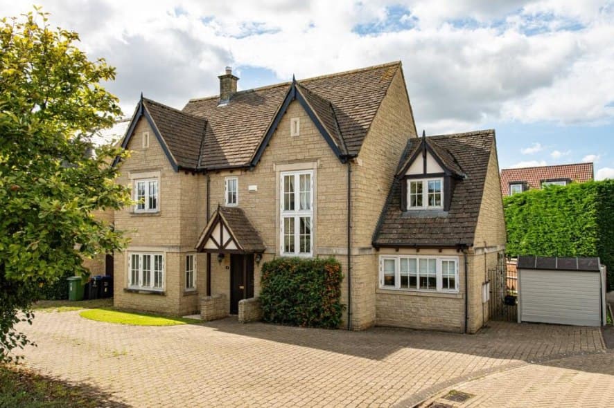 Smallbrook Gardens, Ross-on-Wye: detached cream-and-stone two-storey home with a gabled frontage and attached garage on a block-paved drive among mature trees, WM Housing scheme
