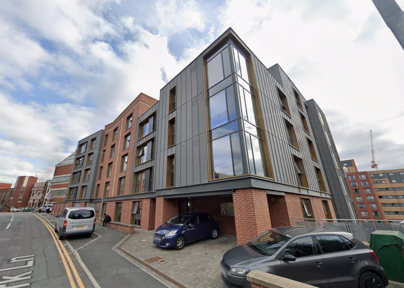St Johns House, Leeds: contemporary four- to five-storey apartment block in grey zinc cladding and red brick with a full-height glazed corner stair and undercroft parking, Leeds and Yorkshire Housing scheme