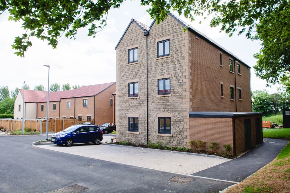 The Moorings, Pucklechurch: three-storey apartment block in Cotswold stone with bin store, parking court and terraced houses beyond