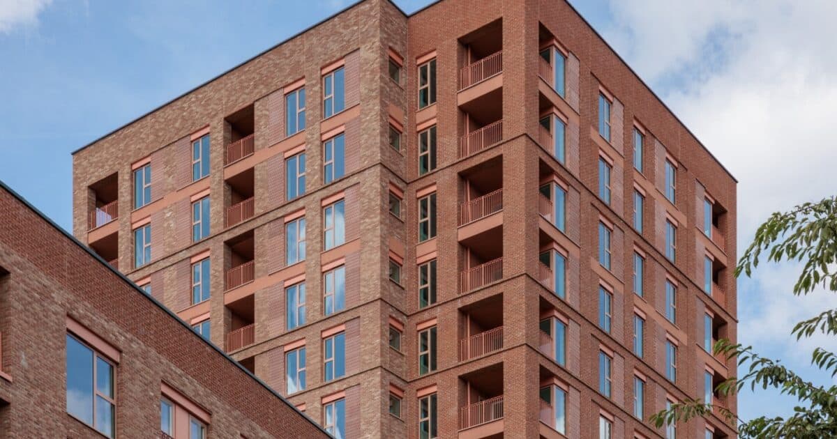 Walter Tull House, Welbourne: close-up of the red-brick tower corner, recessed balconies, brick-soldier window heads and a chamfered building edge against blue sky