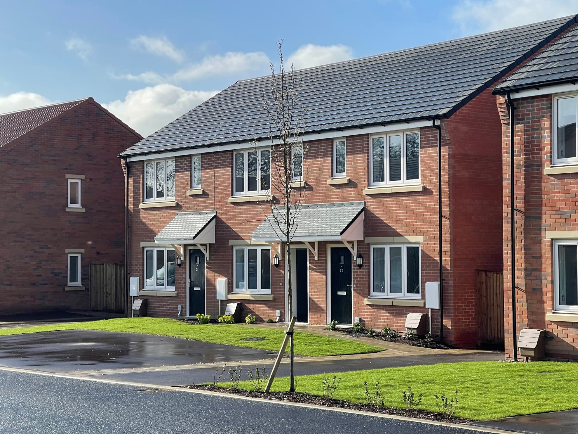 Tower Mill, Necton: completed red-brick three-house terrace with grey pitched roof, brick-soldier window heads and pitched porch hoods, Flagship Homes affordable scheme