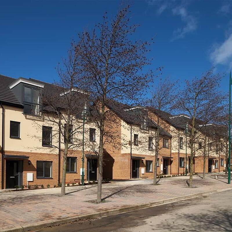 Walton on the Naze (Kirby Road): completed three-storey terrace of cream-rendered townhouses with red-brick base and dormer windows, tree-lined street and block-paved pavement, Flagship Housing affordable scheme