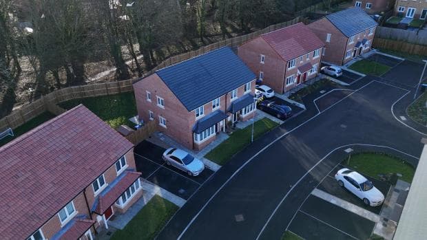 Weavers Close, Peterlee: low-altitude drone view of two red-brick semi-detached pairs at handover, slate pitched roofs and grey window frames, cars on the driveways and adjacent properties visible at the curving estate road