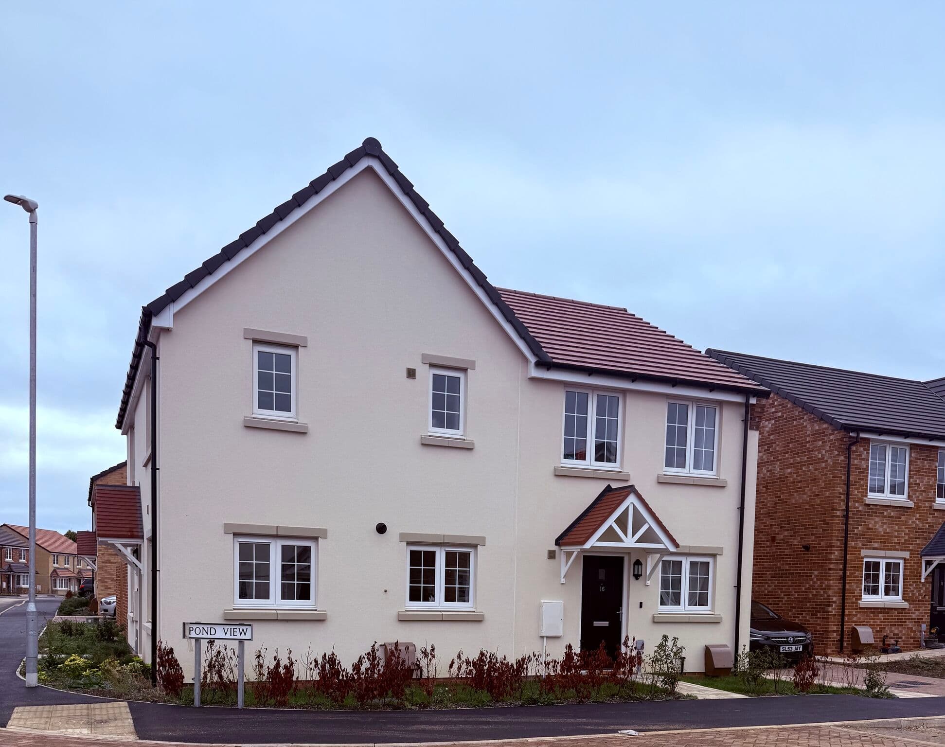 Wisbech Road, March: completed cream-rendered detached house with red-brick base, red-tile pitched roof and white-trimmed porch, "Pond View" street sign in the foreground